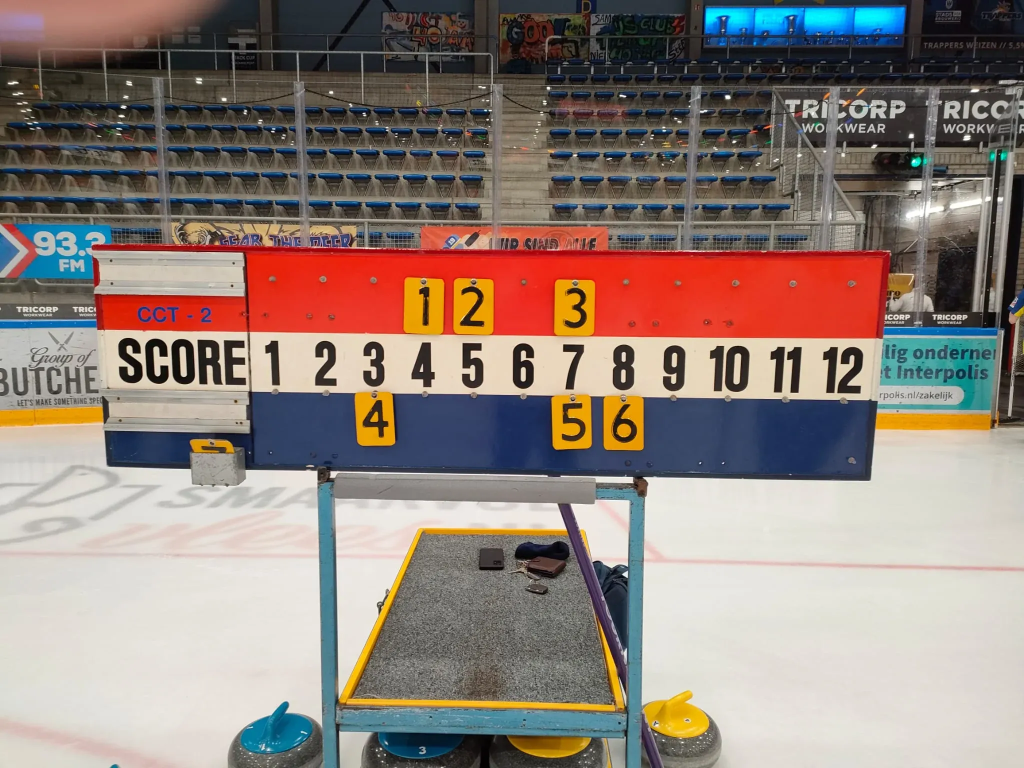 Red, white and blue Curling Club Tilburg scoreboard on a trolley beside the ice